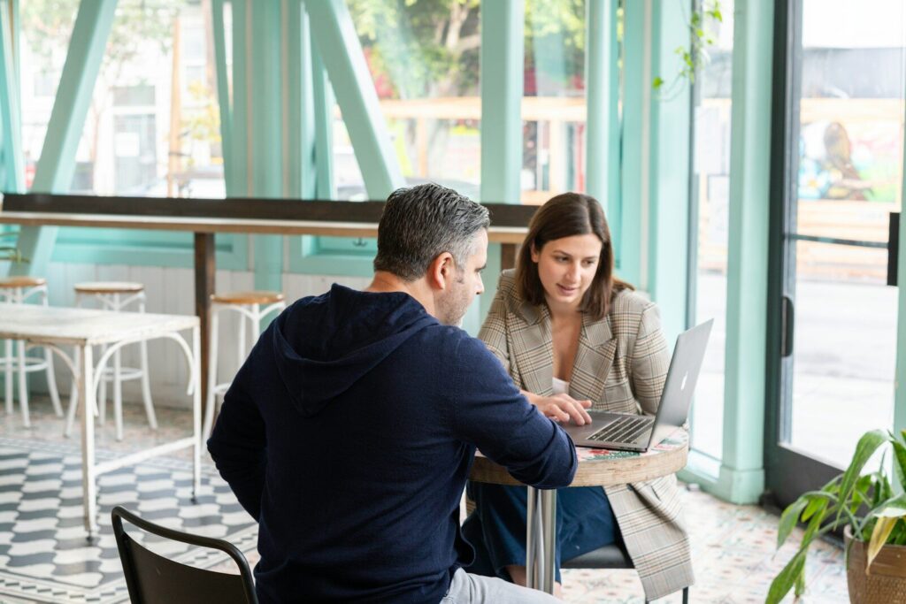 A man and a woman working on a laptop at a cafe table